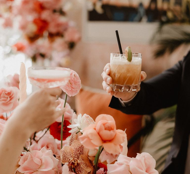 Toasting with pink and peach cocktails over peach wedding flowers