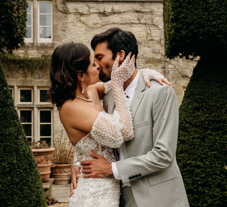 Bride & groom kiss on pathway lined by manicured green trees