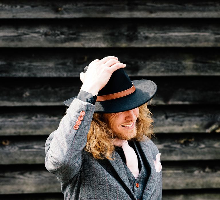 Stylish groom in a grey check suit and black fedora hat 