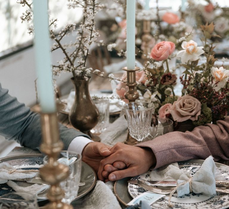 Rustic tablescape with floral decor as grooms reach across to hold hands with one another