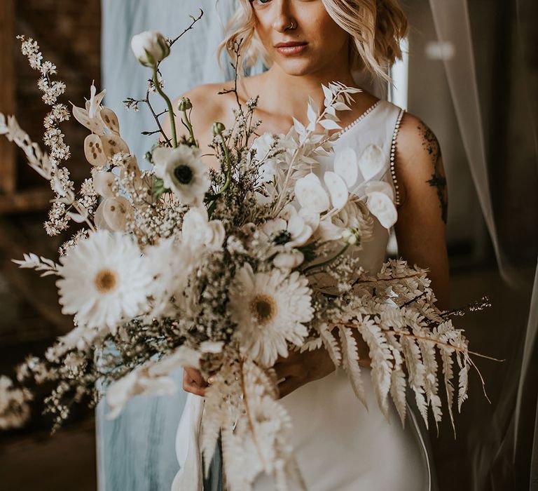 Bride in a one shoulder dress with turban headband holding a white flower wedding bouquet 