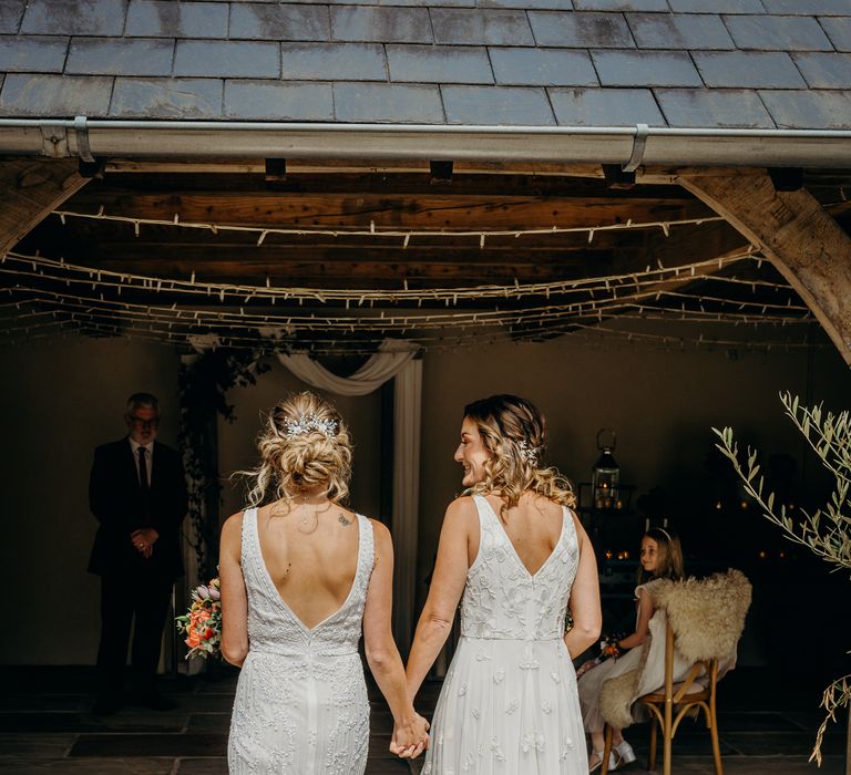 Brides walk together hand in hand on their wedding day as the sun shines