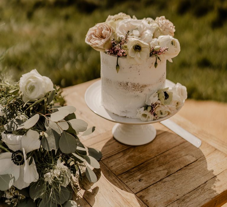 Small white semi-naked wedding cake with floral decor on wooden table at Dunluce Castle Wedding 