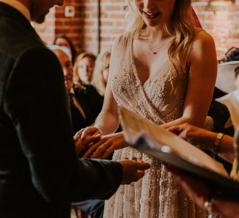  Bride in pearl wedding dress holds hands with groom in checked suit during barn wedding ceremony