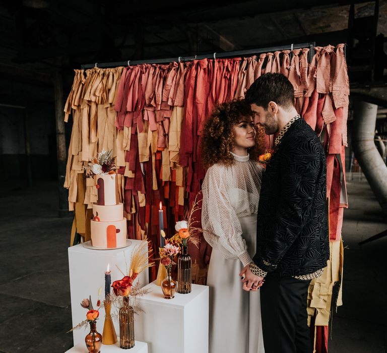 70s wedding inspiration with red to yellow ombre fabric backdrop, iced wedding cake and wildflowers in brown bottles 