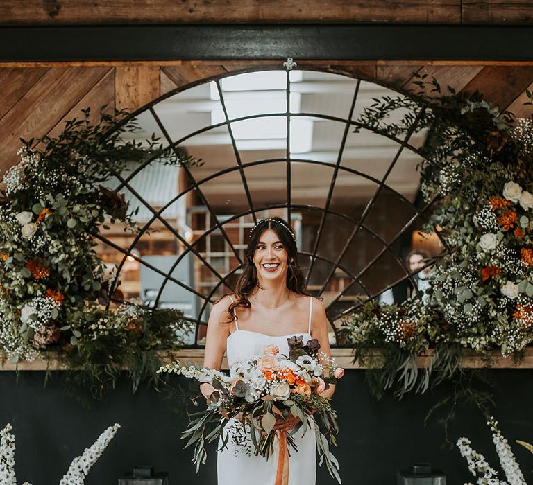 Bride in a Made With Love Carla A-line wedding dress with thin straps standing at the altar of new Lake District wedding venue, Ghyll Barn holding a bridal bouquet tied with ribbon 