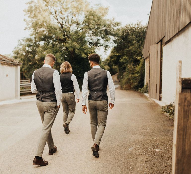 Three groomsmen and groom in sage green trousers, white shirts and silk backed waistcoats walk down country lane at Anran Devon 