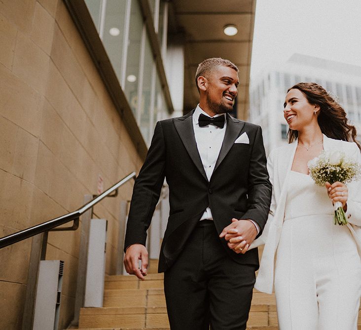 Bride and groom portrait with groom in a black tuxedo and bride in a white suit both from Reiss 