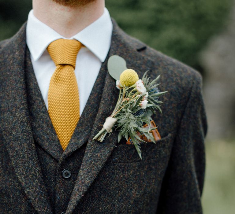 Groom in a wool suit with speckles, yellow tie and billy button buttonhole 