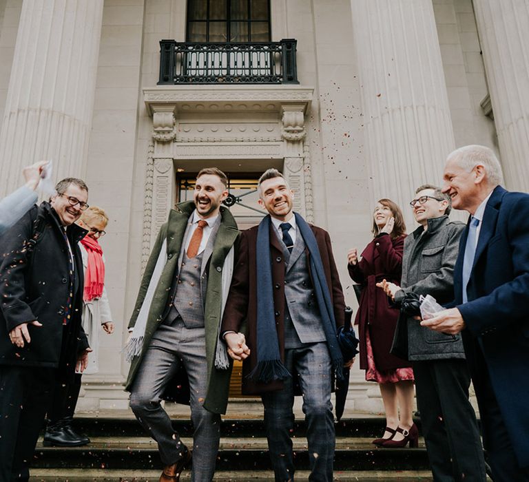 Grooms leave Old Marylebone Town Hall on their wedding day as wedding guests throw confetti around them for December wedding