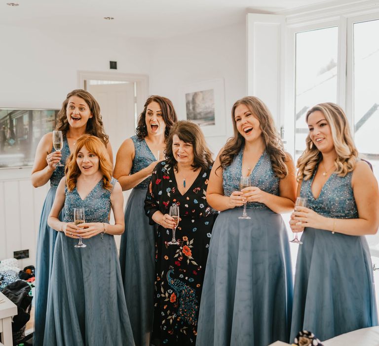 Bridesmaids see bride for the first day on her wedding day as they look and smile whilst wearing blue bridesmaids dresses