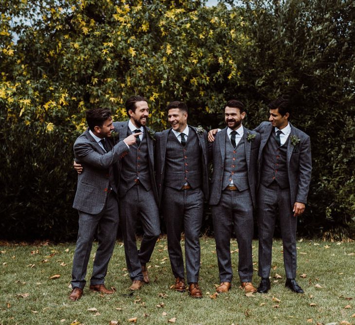 Groomsmen arm in arm in grey three-piece wedding suits with contrasting buttons 