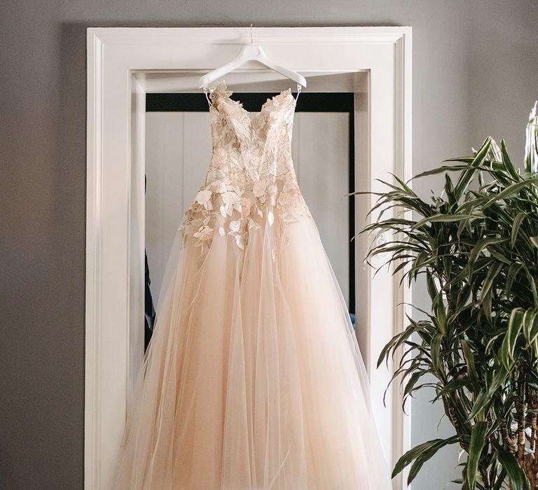 Bridal gown hangs in doorway with appliqué petals and full chiffon skirt 