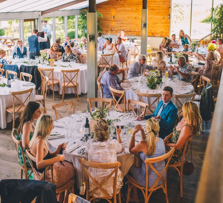 Wedding guests gather indoors for wedding reception complete with hanging fairy lights above | Story + Colour