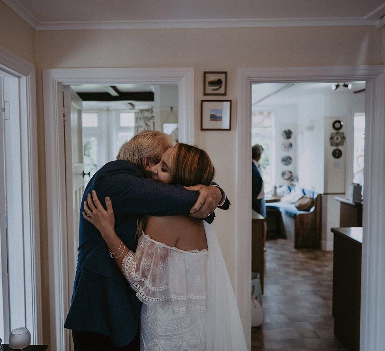 Bride in Grace Loves Lace bardot wedding dress and veil hugs man in blue suit in hallway before Isle of Wight wedding with macrame wedding decor