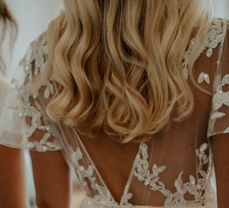 Bride with long wavy blonde hair in a lace and sequin wrap wedding dress by Constellation Ame 