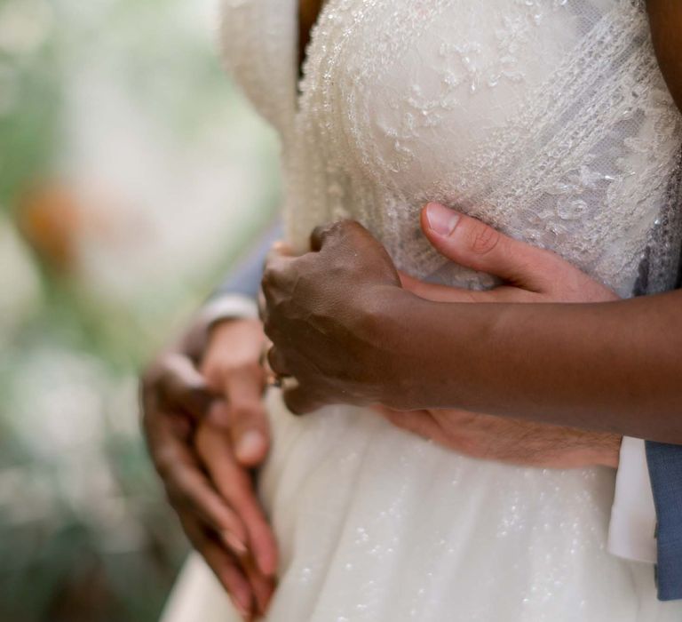 Groom holds his arms around bride as she holds his hand