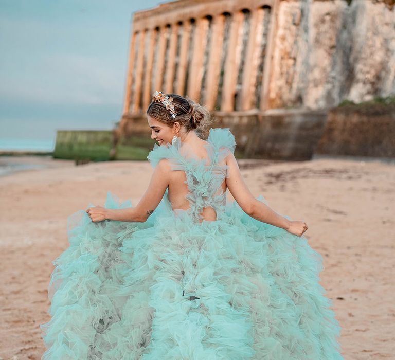 Bride in a layered tulle mint green wedding dress holding out her train on the beach 