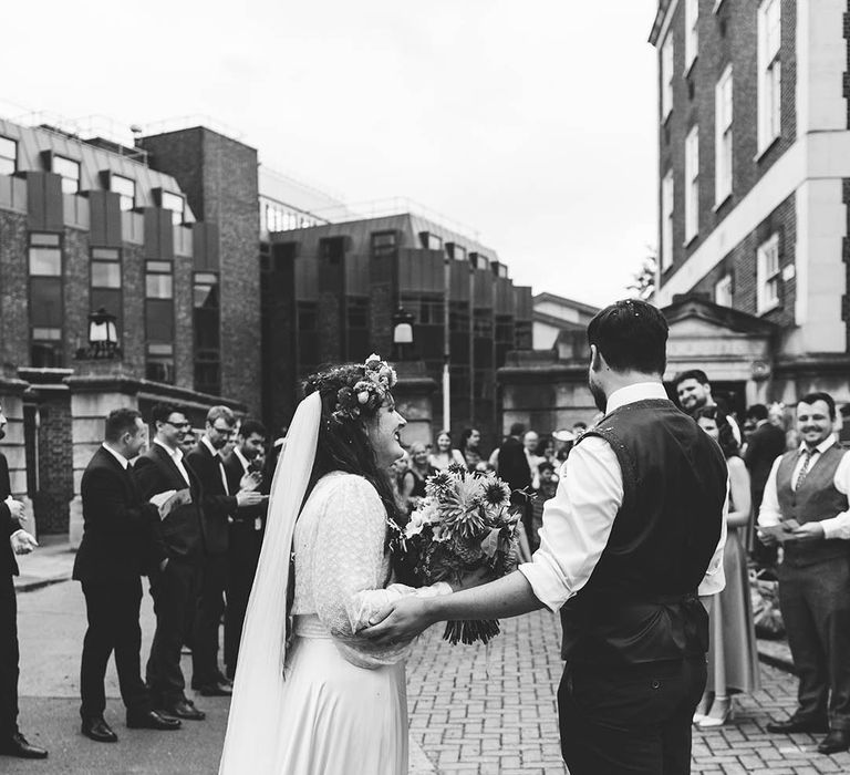 Black & white image of bride and groom holding hands outdoors on their wedding day