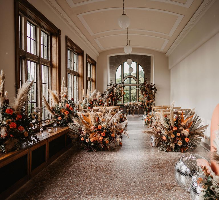 Interior of Kinmount House wedding ceremony room with wooden chairs, orange and green boho floral installations and large windows