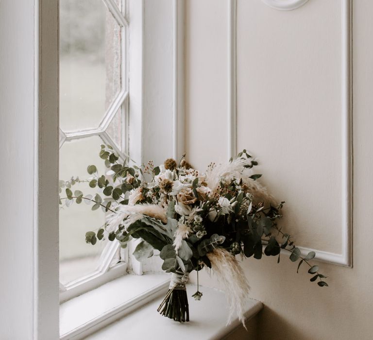 Bridal bouquet placed on windowsill filled with pampas grass and white florals