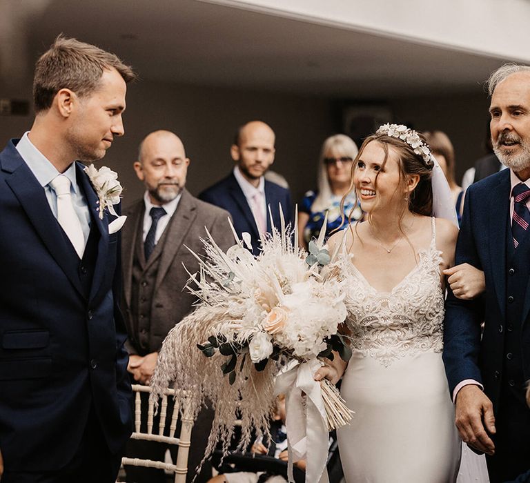 Bride holds dried floral bouquet as she walks down the aisle with her father