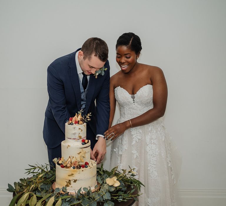 Wedding couple cut three tier wedding cake with fresh eucalyptus and fruit 