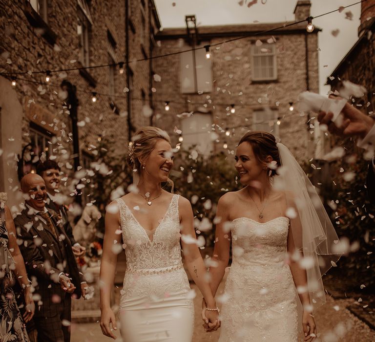 Brides walk together as confetti is thrown around them on their wedding day