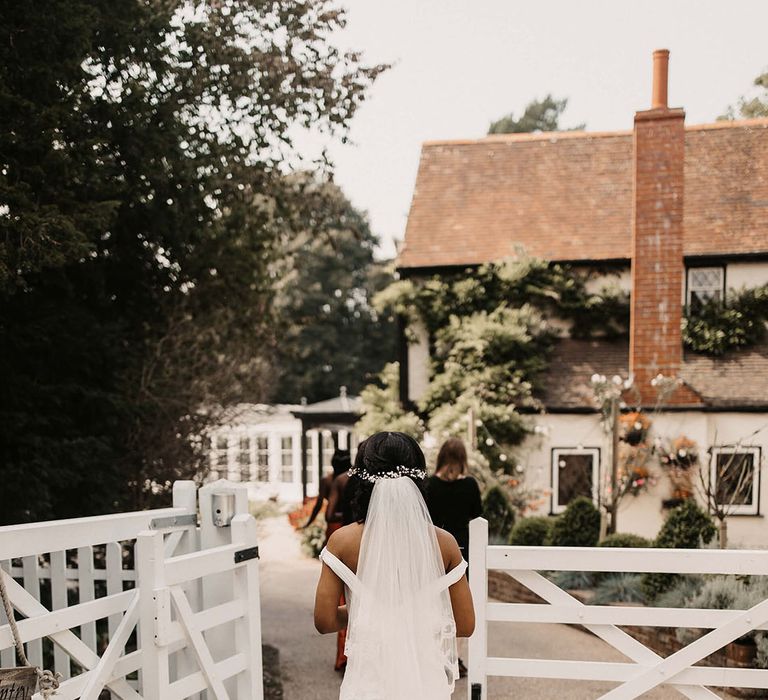 Bride walks through white gate on her wedding day at Haynes House