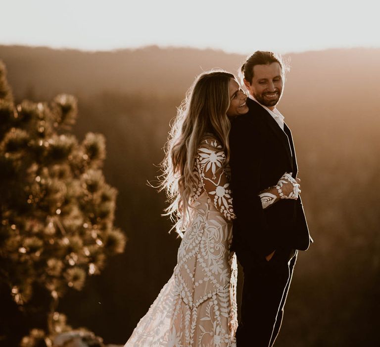 Bride & groom embrace on mountain as the sun sets 