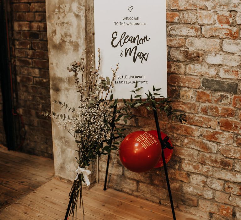 White rustic wedding welcome sign on black easel with dried florals and balloons for industrial style wedding