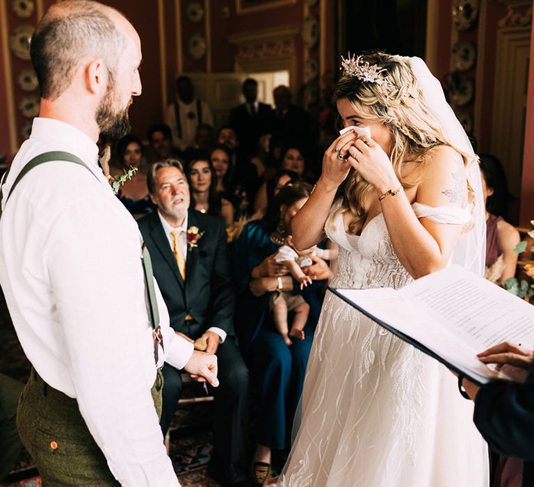 Bride wipes away her happy tears at the end of the aisle with her groom in intimate venue