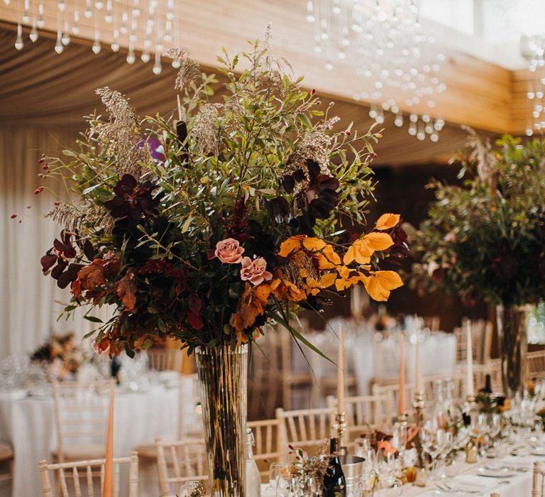 White tablecloth and tables cape complete with large green foliage and nonage and deep red flower centrepieces 