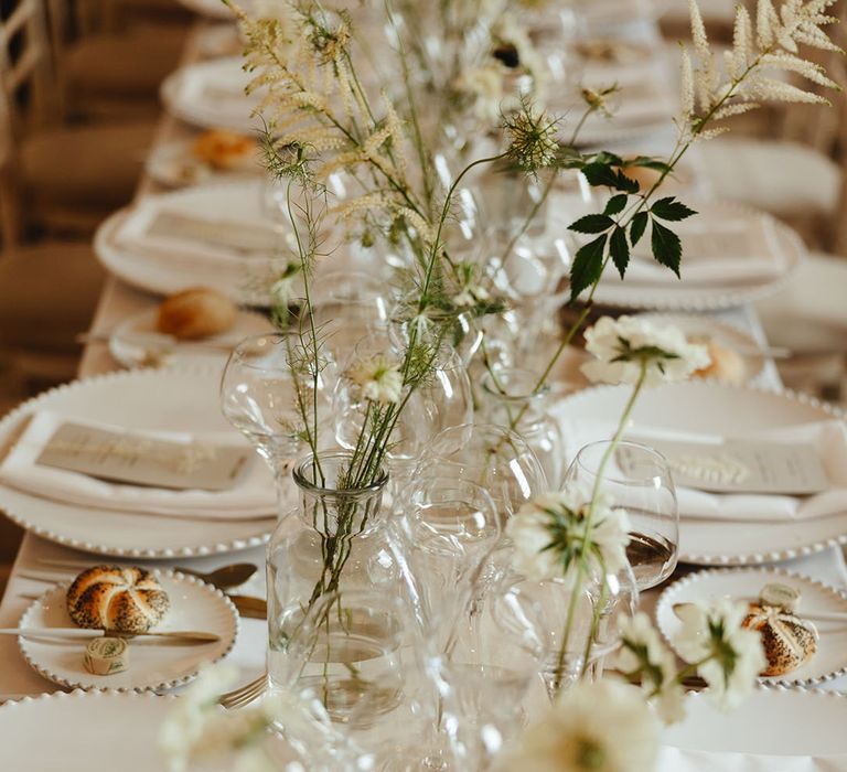 Plate table setting with white plates, napkins, flowers and plain glassware for clean and natural styled wedding