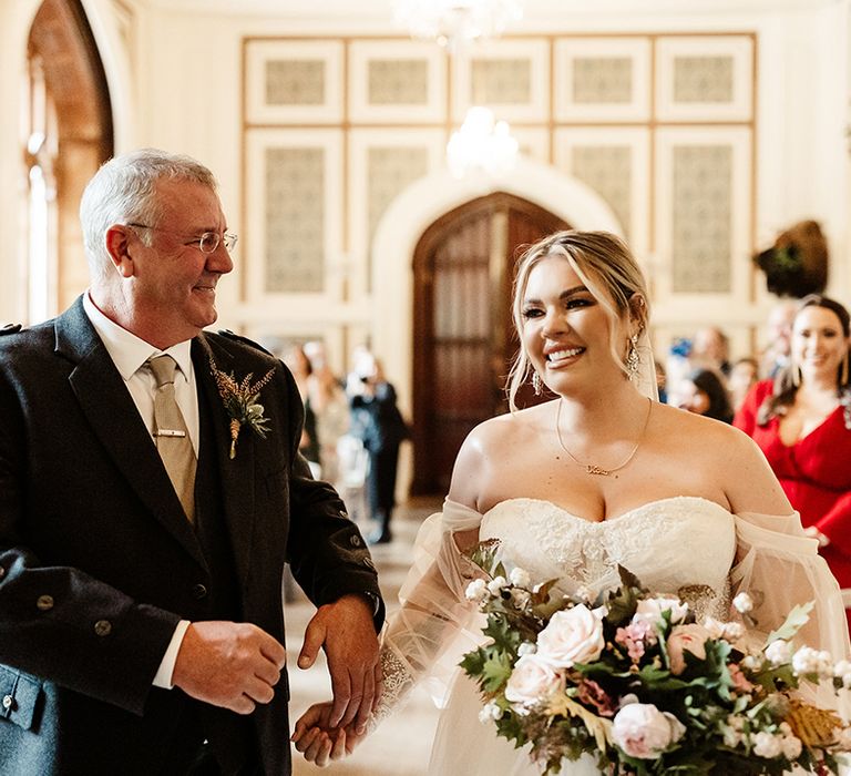 Father of the bride in dark suit jacket and beige tie with silver tie clip gives away the bride in strapless wedding gown 