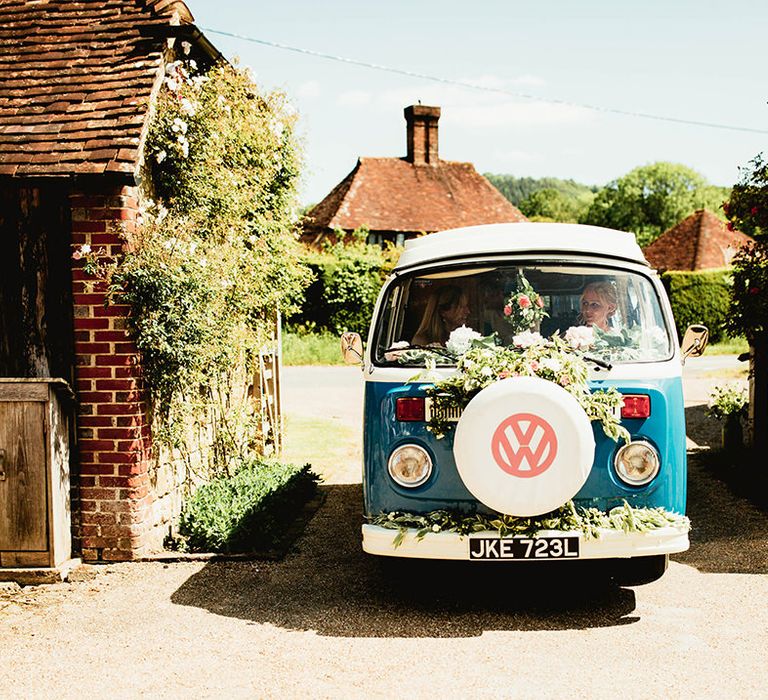 Bride entering in vintage Volkswagen camper van decorated with flowers for boho outdoor home wedding