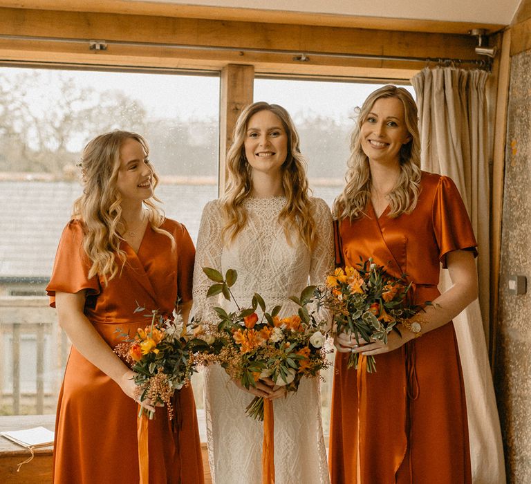 Bride in lace Rosa Clara wedding dress with bridesmaids in burnt orange wrap satin Rewritten dresses with autumnal bouquets