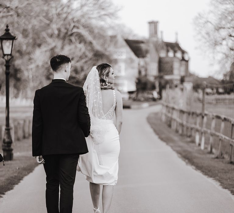 Groom lifts up the train of the bride's dress as they both walk to the reception