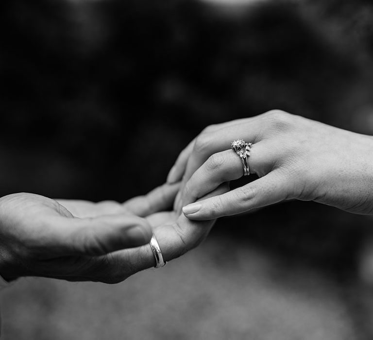 Bride and groom hold hands to show off their rings with bride wearing wishbone wedding ring and round engagement ring and groom's plain wedding band 