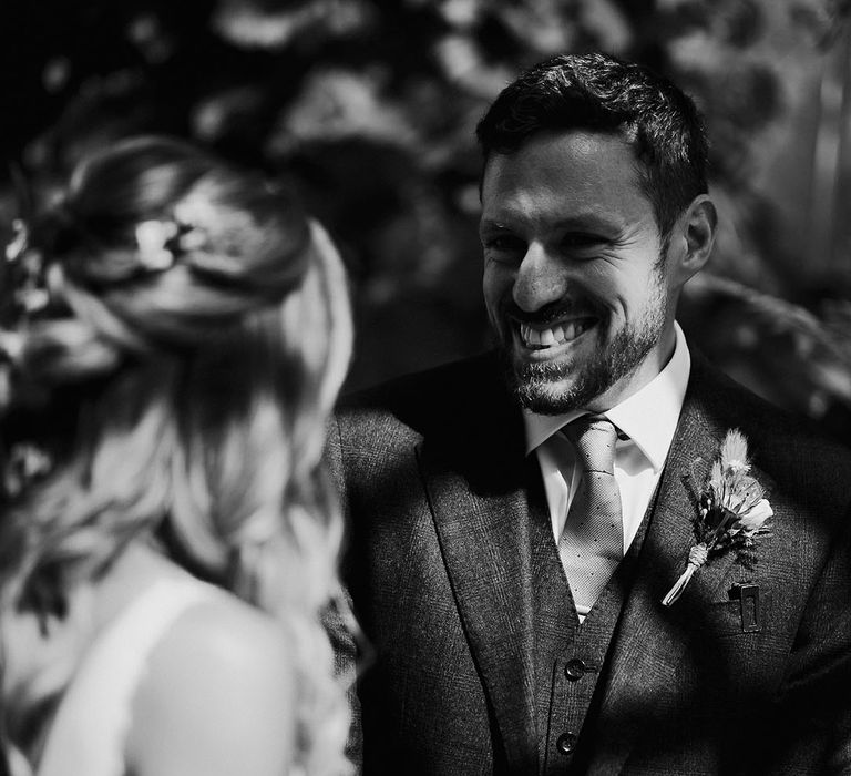 Groom in three piece suit and spotted tie smiling at the bride 