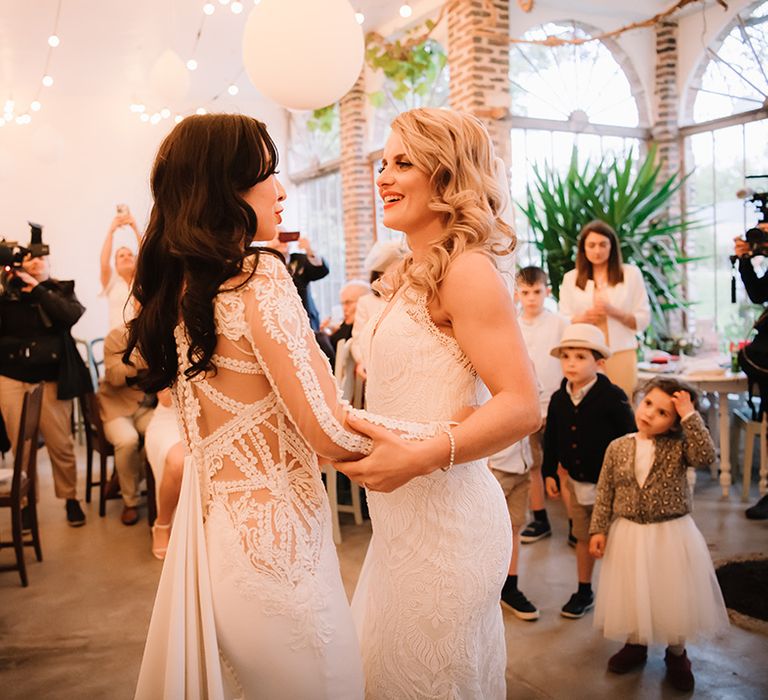 Brides share their first dance together while wedding guests watch 