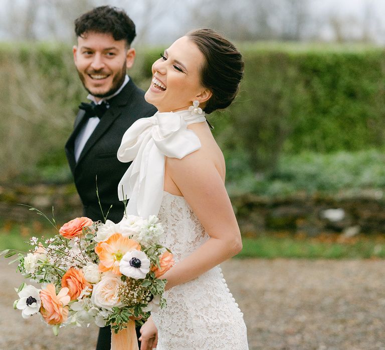 Bride in a halterneck lace wedding dress with satin bow neck detail laughing 