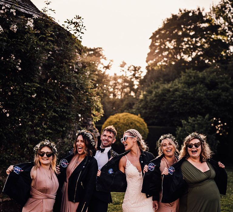 Bride in retro heart sunglasses with bridesmaids in pink and green dresses and groom all in matching NASA leather jackets 