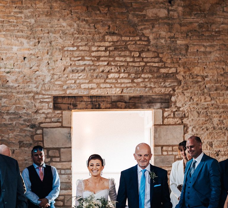 Father of the bride with bright blue tie and handkerchief walks the bride in a ruffle tulle princess skirt wedding dress down the aisle 