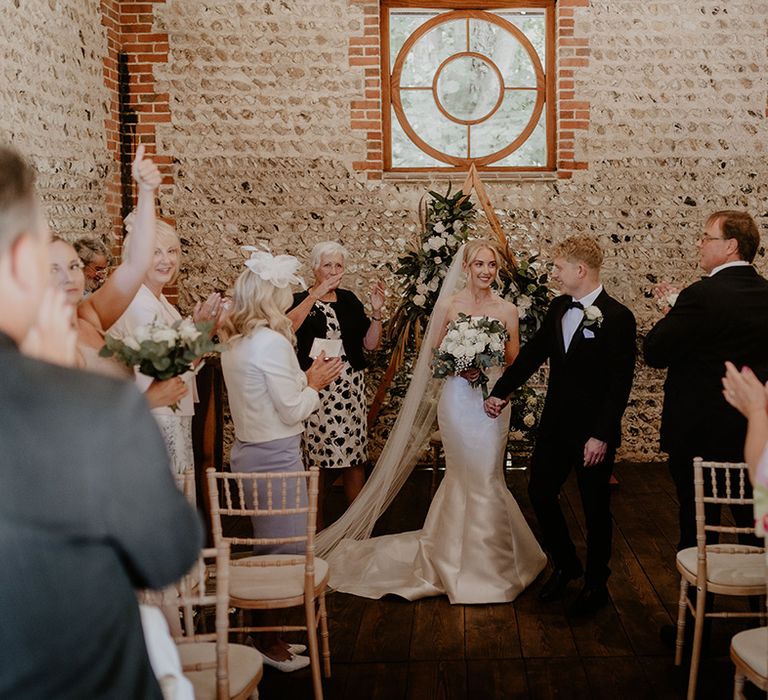 Groom in black tie with bride in strapless dress start to walk back down the aisle as a married couple 