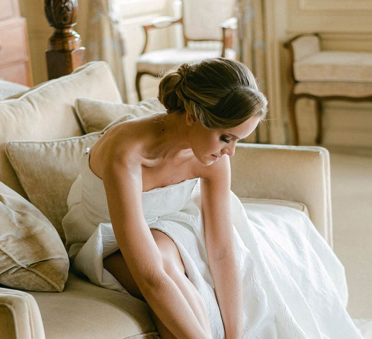 Bride with a sleek updo wears a strapless Jesus Peiro wedding dress putting on pearl wedding shoes