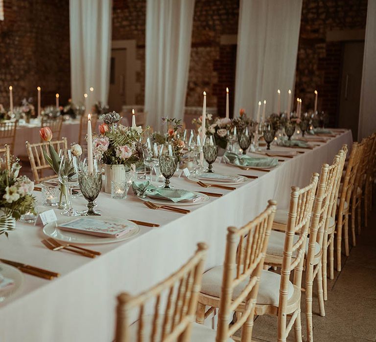 Pale pink taper candles with green glassware and tulips and other pink and white flowers 