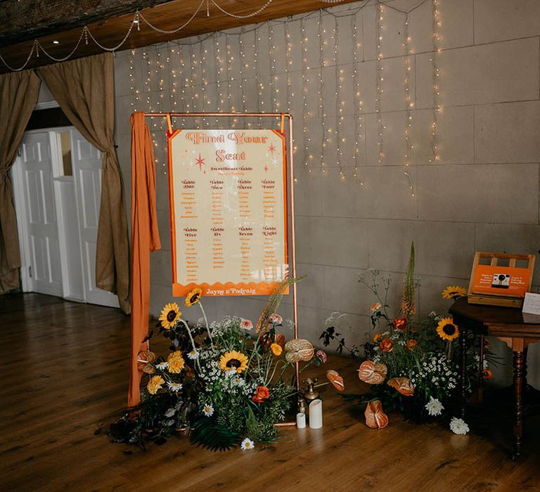 Orange and red table plan with orange and yellow wedding flowers with polaroid camera for guest book 