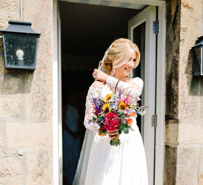 Bride wears lace Pronovias wedding dress and carries bright floral bouquet filled with sunflowers and pink rose 