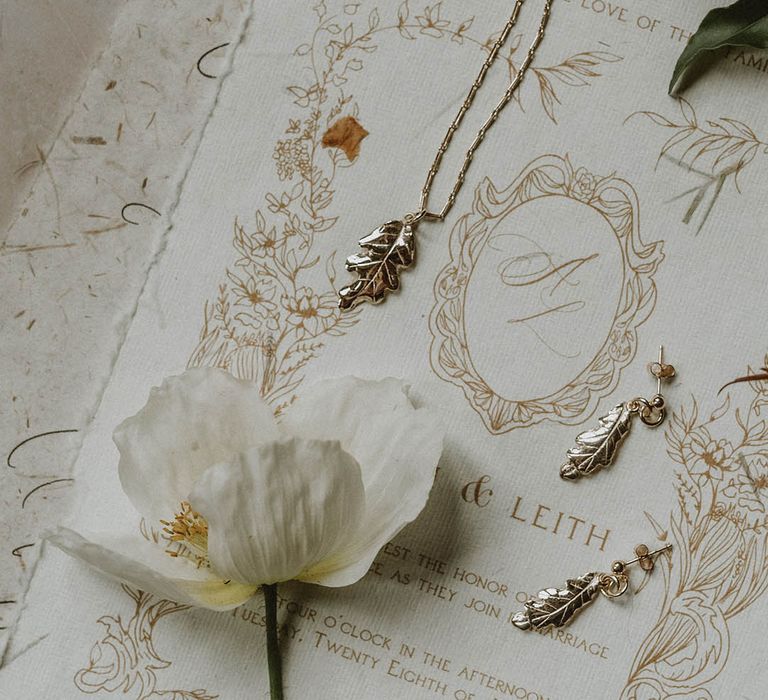 delicate leaf necklace and earrings resting on the vintage-style wedding stationery 